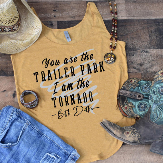 You Are The Trailer Park I Am The Tornado Screen Print Transfer, flat lay of a yellow tank top featuring the quote, with cowboy hat, jewelry, boots, jeans, and a beaded necklace around it on wooden background