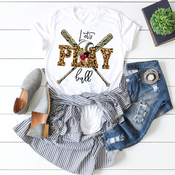 Baseball Lets Play Ball Leopard Sublimation Transfer, a white t-shirt with a leopard print 'PLAY' text, baseball graphics, and crossed baseball bats, displayed with denim shorts, striped skirt, and casual shoes.