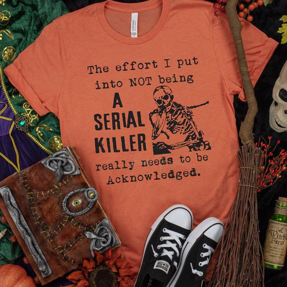 The Effort I Put Into Not Being a Serial Killer Screen Print Transfer T-shirt, orange with black skull and text design.