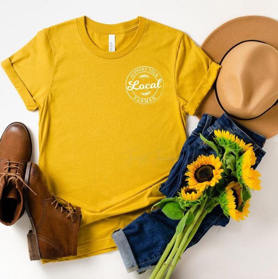 Support Local Pocket Print Heat Transfer, yellow T-shirt with support local farmer logo, brown boots, beige hat, blue jeans, and sunflowers.