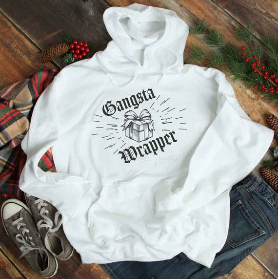 Gangsta Wrapper Black Sublimation Transfer, white hoodie with a gift box graphic and text, on wooden surface with holiday decorations