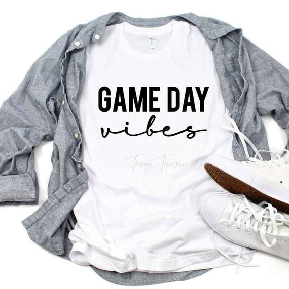 Game Day Vibes Sublimation Transfer, white T-shirt with black and cursive text, laid on a gray shirt with sneakers.