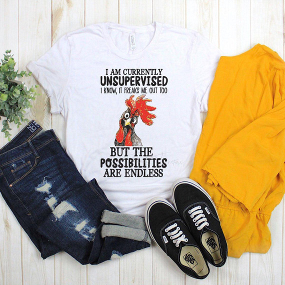 Currently Unsupervised Chicken Sublimation Transfer, white T-shirt with a humorous chicken graphic and text on a flat lay of casual jeans, black Vans sneakers, and yellow clothing on a wooden background.