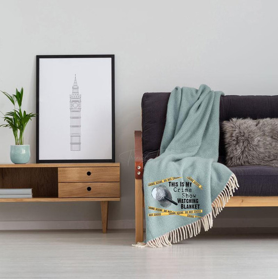This Is My Crime Watching Blanket Screen Print Heat Transfer, light blue blanket with crime show print draped over a dark sofa in a modern living room.