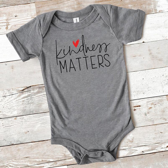 Kindness Matters INFANT Screen Print Heat Transfer, gray infant onesie with 'kindness MATTERS' text and a red heart above the 'i' on a wooden background.