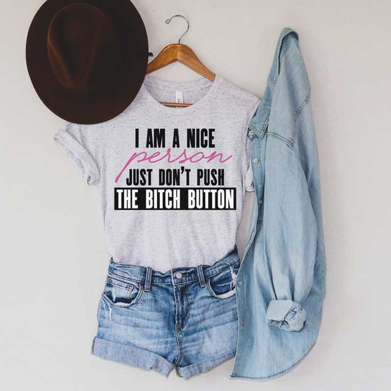 I Am A Nice Person Sublimation Transfer, casual outfit with a printed t-shirt, denim shorts, a denim shirt, and a brown hat hanging on a wall.