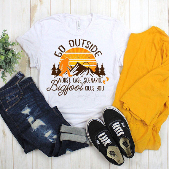 Go Outside Worse Case Scenario Bigfoot Kills You sublimation transfer t-shirt with outdoors and Bigfoot design, paired with ripped jeans, black Vans sneakers, and a yellow jacket.