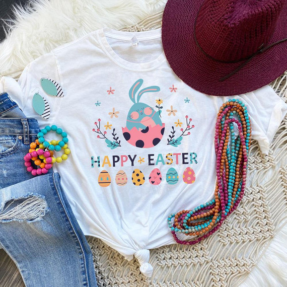 Happy Easter Sublimation Transfer, Easter-themed design on a white T-shirt with bunny and decorated eggs, surrounded by colorful jewelry, hat, and denim jeans.