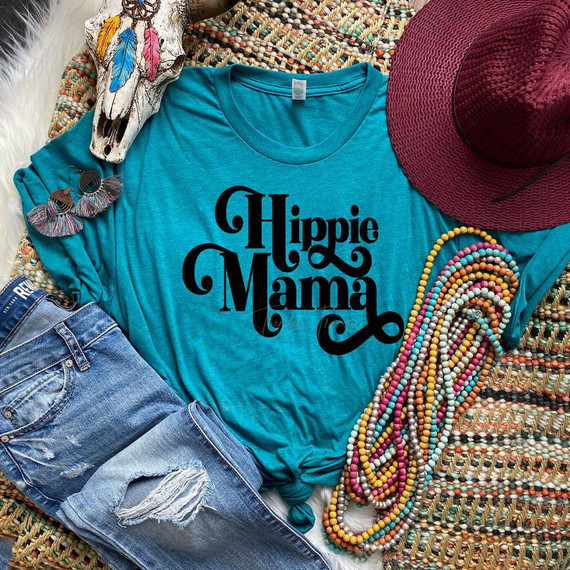 Hippie Mama Screen Print Heat Transfer, turquoise t-shirt with Halloween-inspired typographic design, surrounded by colorful accessories including beads, a maroon hat, earrings, and decorative feathers.