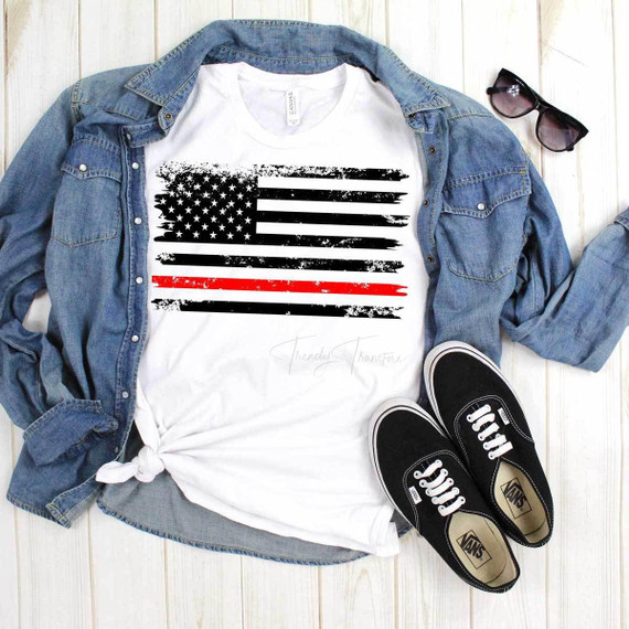 Flag With Thin Red Line Sublimation Transfer, a graphic T-shirt featuring a black and red American flag design with a distressed style, laid on a wooden surface with a denim jacket, sunglasses, and Vans shoes.