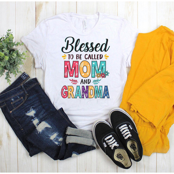 Blessed To Be Called Mom And Grandma Sublimation Transfer, colorful graphic T-shirt with the text 'Blessed to be called Mom and Grandma' displayed on it, surrounded by jeans, yellow jacket, sneakers, and a small plant on a wooden surface.