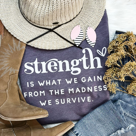 Strength is What We Gain Screen Print Heat Transfer, motivational slogan on purple fabric with accessories like a straw hat, earrings, yellow flowers, and denim jeans arranged around it.