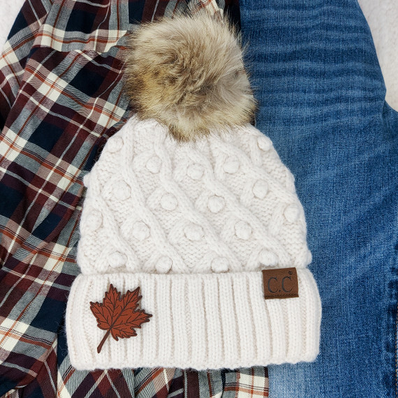 Falling Leaf Leather Patch, a brown leather patch with a falling leaf design sewn onto a white knit beanie.