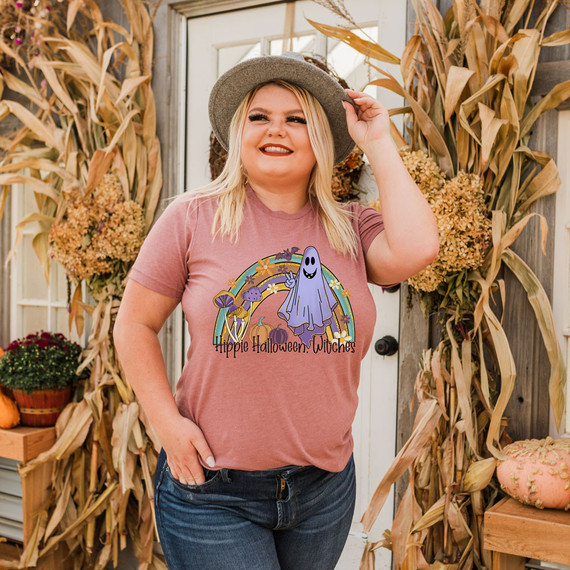 Hippie Halloween Witches DTF Heat Transfer, woman wearing a Halloween-themed t-shirt with a ghost, rainbow, mushrooms, pumpkins, and flowers design.