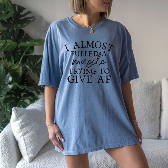 T-shirt, a woman wearing a blue T-shirt with the humorous message 'I Almost Pulled A Muscle Trying To Give AF' printed on it.