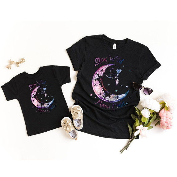 Stay Wild Moon Child DTF, matching family T-shirts with a moon and star design and the words "Stay Wild Moon Child" on a white background with flowers, sunglasses, and gold shoes.