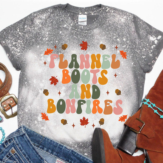 Flannel Boots and Bonfires DTF Transfer, a colorful graphic design printed on a gray tie-dye T-shirt featuring fall leaves, acorns, and the phrase "Flannel Boots and Bonfires" in vibrant autumn colors.