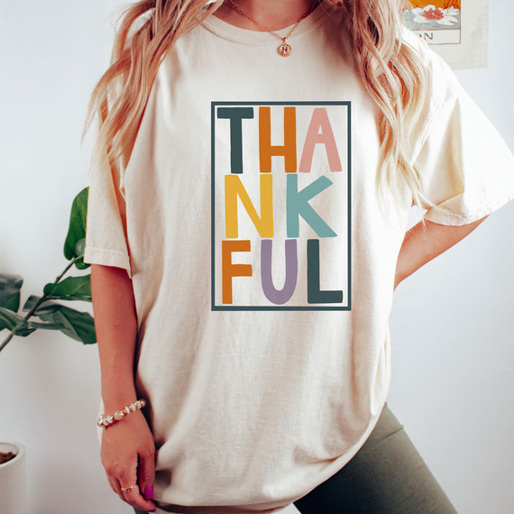 Thankful DTF Transfer, colorful thank you message graphic on a beige t-shirt worn by a woman.
