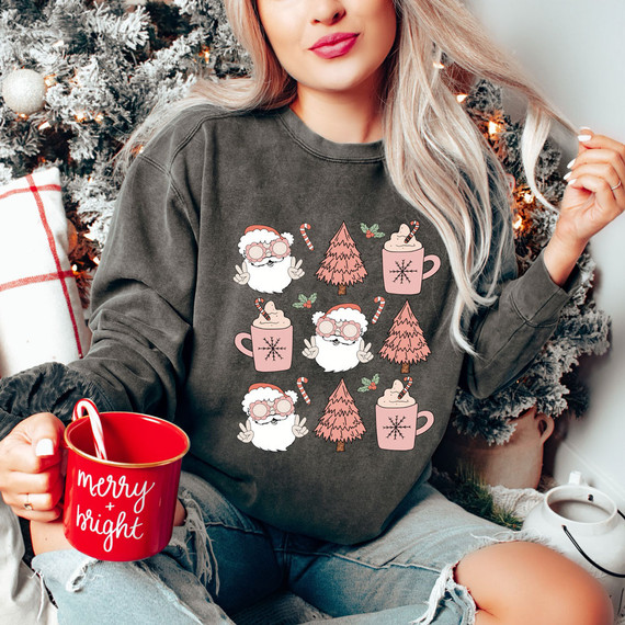 Retro Christmas DTF Transfer, festive holiday-themed design featuring Santa Claus, Christmas trees, candy canes, and mugs of hot cocoa on a woman's sweatshirt, with a Christmas tree and decorations in the background.