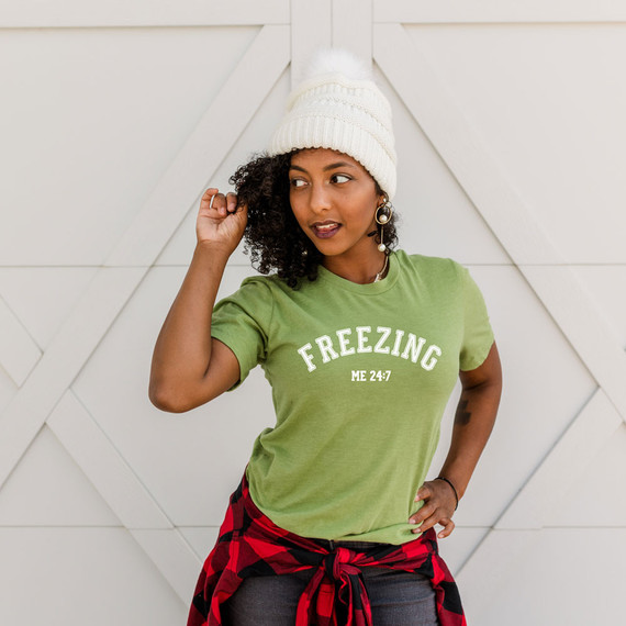 Freezing 24:7 DTF Transfer, woman wearing green T-shirt with white text and beanie hat.