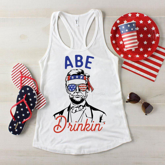 Abe Drinkin' Patriotic Sublimation Transfer, a tank top with a patriotic design featuring Abraham Lincoln wearing American flag-themed sunglasses and a headband, surrounded by red, white, and blue accessories with stars and stripes.