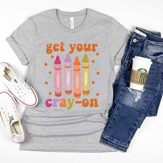 Get Your Cray-On DTF Heat Transfer, gray t-shirt with colorful crayon graphic and text, casual jeans, and a Starbucks coffee cup.