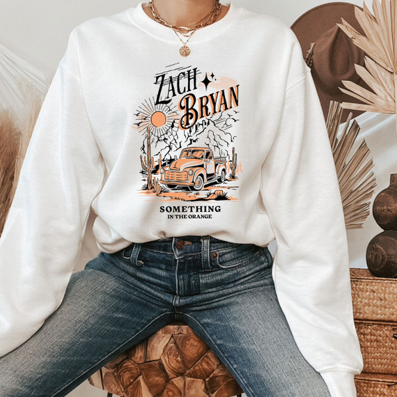 Zach Something In The Orange DTF Heat Transfer, graphic design of a vintage truck in a desert landscape with cacti, mountains, sun and stars, printed on a white sweatshirt.
