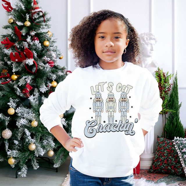 Let's Get Crackin' DTF Heat Transfer, a girl wearing a festive sweatshirt with nutcracker soldiers design during Christmas celebration.