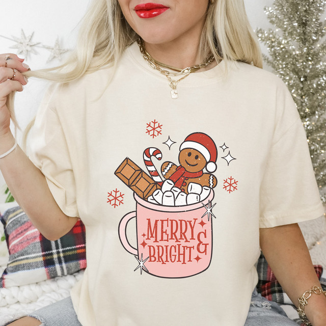 Merry & Bright Gingerbread DTF Heat Transfer, a festive gingerbread man in a Santa hat in a pink mug filled with marshmallows, candy cane, and chocolate bar, with holiday-themed accents.