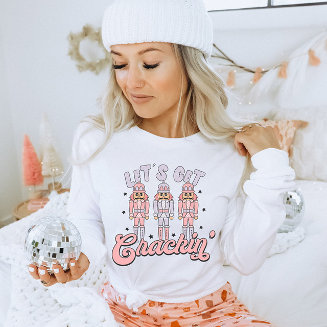 Let's Get Crackin' Pink DTF Heat Transfer, woman wearing a white shirt with pink nutcracker design, cozy holiday setting.