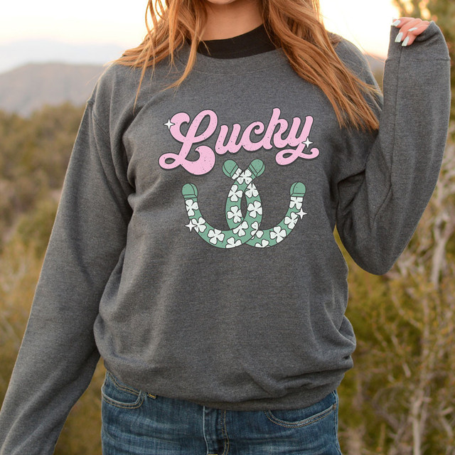 Lucky Horseshoe DTF Heat Transfer, a graphic design featuring the word 'Lucky' in pink cursive with a sparkling effect and a green horseshoe decorated with shamrocks and hearts.