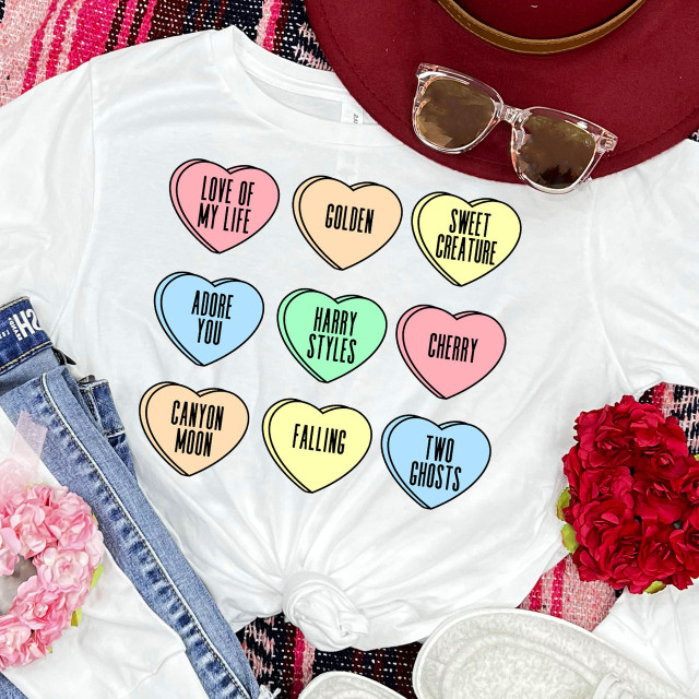 Styles Candy Hearts DTF Heat Transfer, colorful heart-shaped designs with words like 'LOVE OF MY LIFE', 'GOLDEN', 'SWEET CREATURE', 'ADORE YOU', 'HARRY STYLES', 'CHERRY', 'CANYON MOON', 'FALLING', and 'TWO GHOSTS' on a white t-shirt.