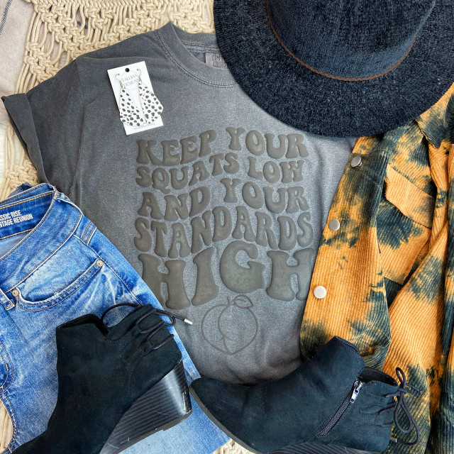Keep Your Squats Low PUFF Screen Print Heat Transfer, a gray T-shirt with the motivational quote in puff black lettering, surrounded by accessories including a black hat, tie-dye shirt, denim jeans, black boots, and black gloves.