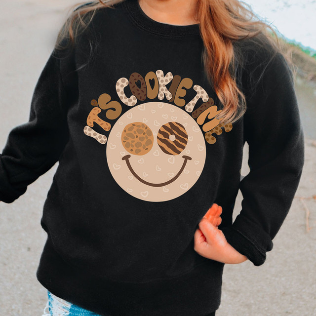 It's Cookie Time DTF Heat Transfer, black sweatshirt with a cute smiling face design featuring cookie-themed eyes and the text 'It's Cookie Time' in colorful chocolate and cookie patterns.