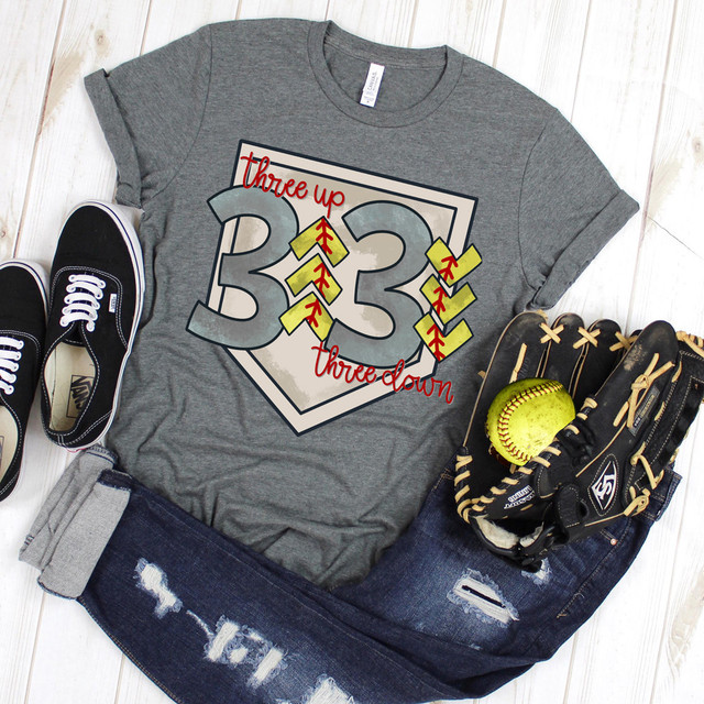 Three Up Three Down Softball DTF Heat Transfer, displayed on a gray T-shirt with baseball and softball accessories around it.