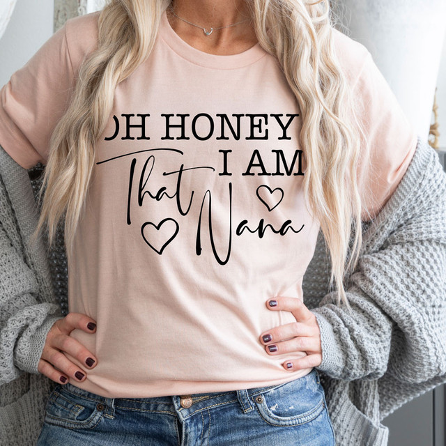 Oh Honey, I Am That Nana DTF Heat Transfer - Woman wearing a pink T-shirt with a black and script 'Oh Honey, I Am That Nana' design, featuring hearts, showcasing custom heat transfer print.