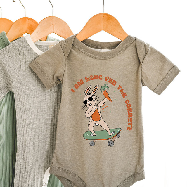 I Am Here For The Carrots DTF Heat Transfer - Cute bunny graphic on a onesie, holding a carrot and wearing sunglasses with playful text, displayed on a hanger.