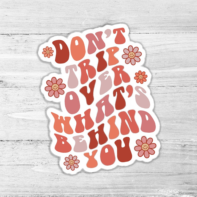 Don't Trip Over What's Behind You Die Cut Sticker, colorful motivational quote sticker with flower illustrations on a wooden background.