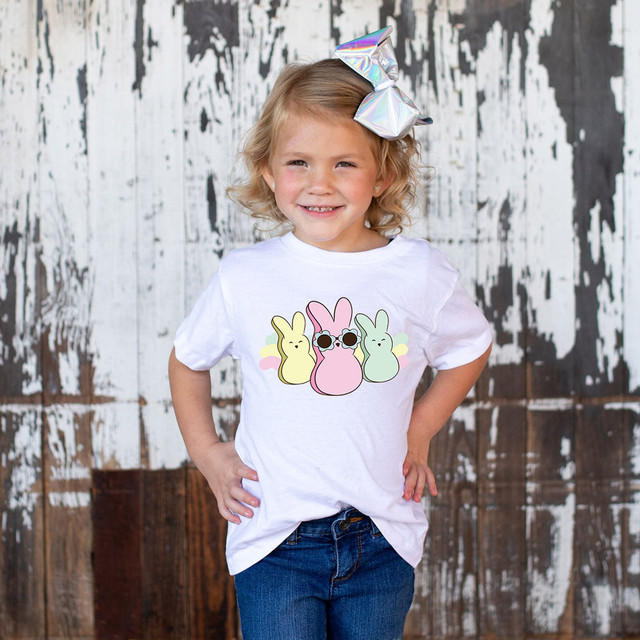 Retro Bunnies DTF Heat Transfer, a vibrant design featuring three pastel-colored bunnies with one in the middle wearing sunglasses, applied on a white T-shirt worn by a smiling young girl.