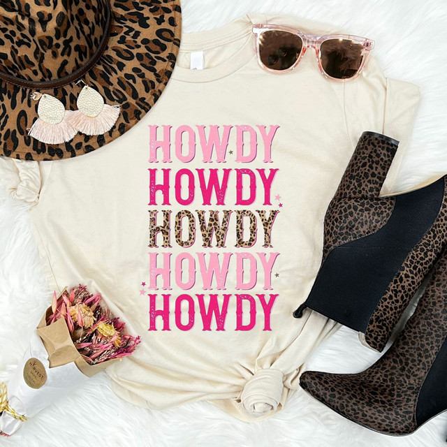 Howdy Leopard Stacked DTF Heat Transfer, product image showing a white T-shirt with pink and leopard print text, accompanied by leopard print hat, pink sunglasses, leopard print boots, and a small bouquet of pink flowers.