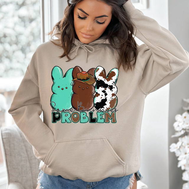 Some Bunnies Problem DTF Heat Transfer, a printed design featuring three cute cartoon bunnies with the text 'Some Bunnies Problem' on a woman's beige hoodie.