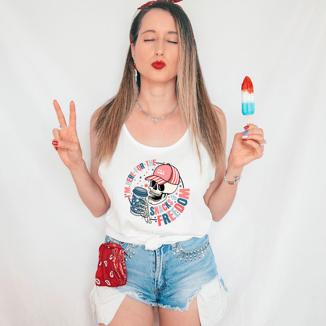 I'm Here For The Snacks & Freedom DTF Heat Transfer, woman wearing tank top with logo, holding ice pop, making peace sign, patriotic summer style.