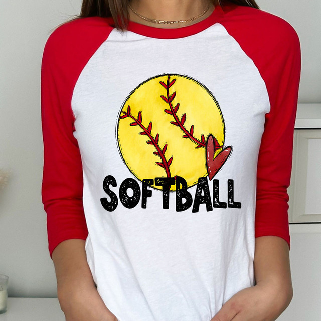 Softball Heart DTF Heat Transfer, yellow softball with red stitches and a red heart, and the word SOFTBALL in bold black letters on a women's raglan shirt.