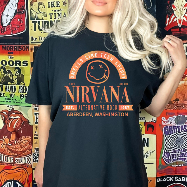 Band Tee NV DTF Heat Transfer, Coral-colored design featuring Nirvana band logo, smiley face with crossed-out eyes, and band details from Aberdeen, Washington, on a black t-shirt worn by a woman with blonde hair.
