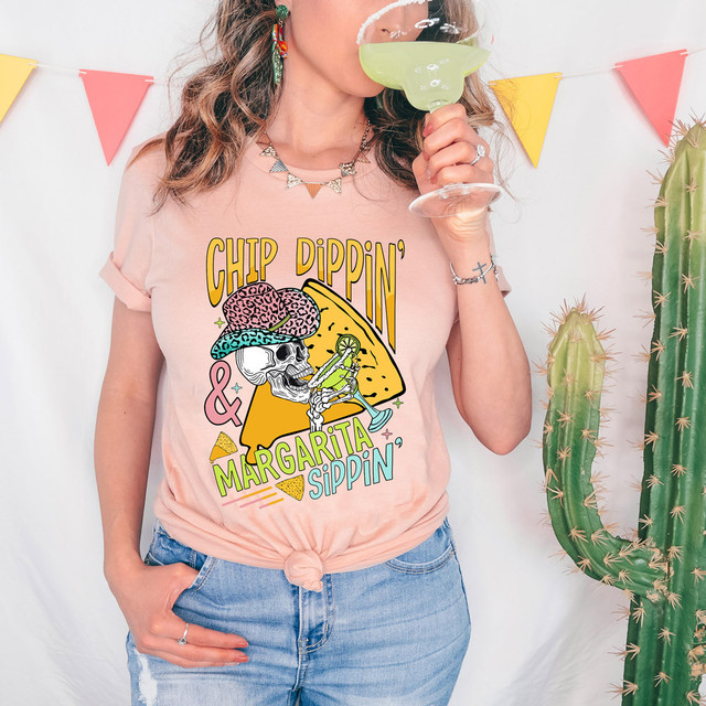 Chip Dippin' & Margarita Sippin' DTF Heat Transfer, colorful graphic design with a skeleton wearing a brain hat and drinking a margarita, on a light pink t-shirt.