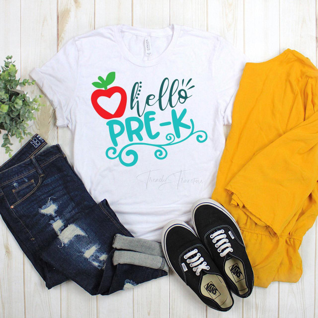 Hello Pre-k Back To School Sublimation Transfer on a white T-shirt, with a playful apple and heart design, paired with distressed jeans, black sneakers, and a yellow jacket, laid out on a light wooden background.