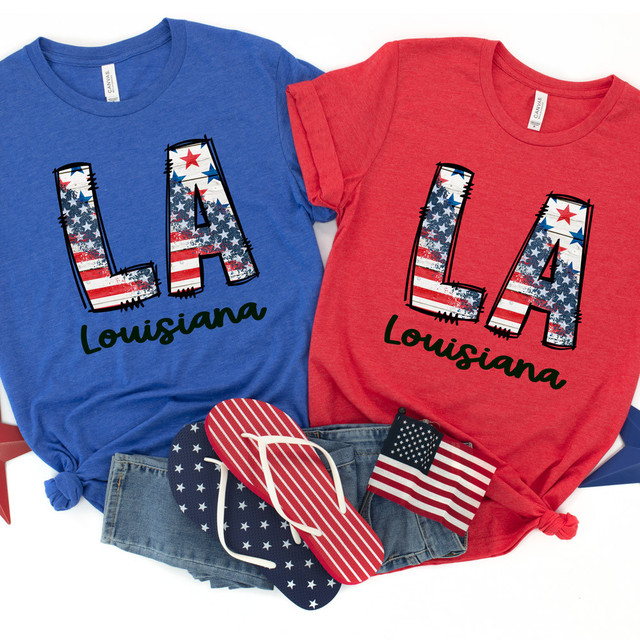 LA Stars & Stripes DTF Heat Transfer, with the design featuring an American flag pattern on the large 'LA' letters and the word 'Louisiana' underneath, displayed on two T-shirts in red and blue.