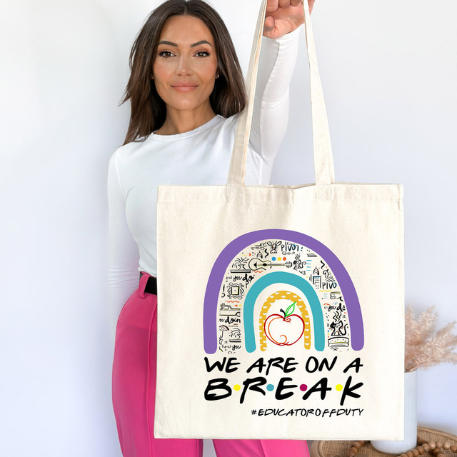 We Are On A Break #EducatorOffDuty DTF Heat Transfer tote bag with colorful rainbow and apple design, held by a woman in a white top and pink pants.