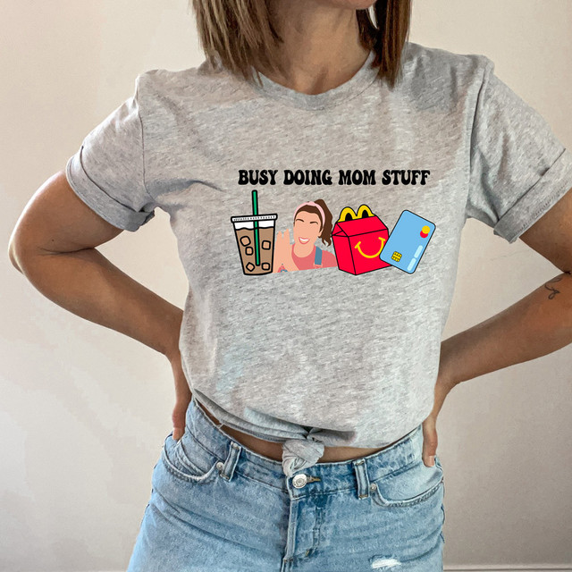 Busy Doing Mom Stuff SFL DTF Heat Transfer, graphic T-shirt with cartoon illustrations of a coffee drink, a smiling woman, a shopping bag, and a credit card.