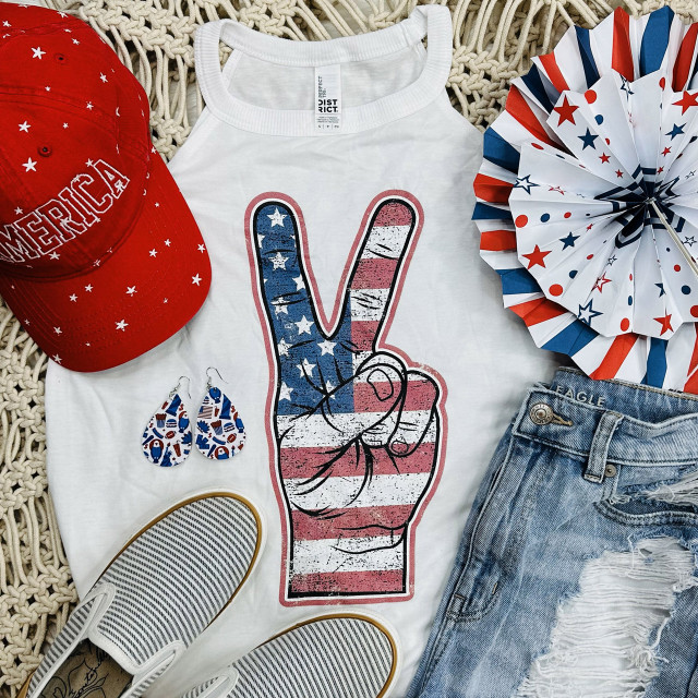 American Peace Distressed Screen Print Heat Transfer, patriotic American flag-themed print of a hand making a peace sign on a white tank top, with red, white, and blue accessories surrounding it.